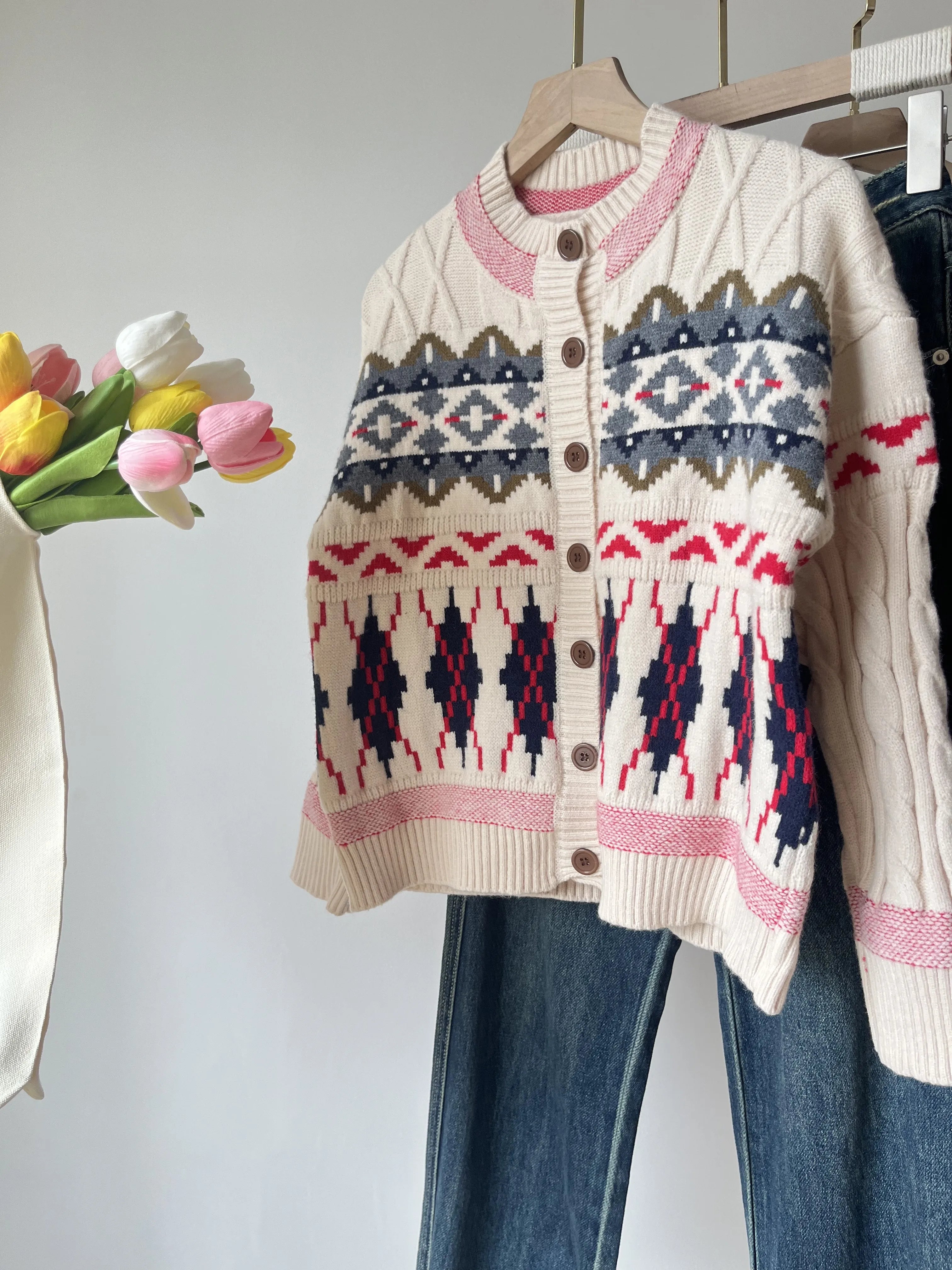Knitted cardigan with geometric pattern on a hanger, next to tulips.