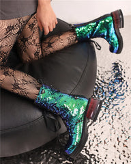 Green sequin boots worn with a patterned shoe and black chair.