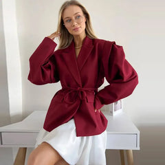 Woman wearing a burgundy blazer with puff sleeves in a minimalistic setting