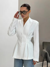 Woman wearing a white blazer and blue jeans indoors.