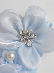 Light blue flower accessory with a central gemstone and pearl on a light gray background