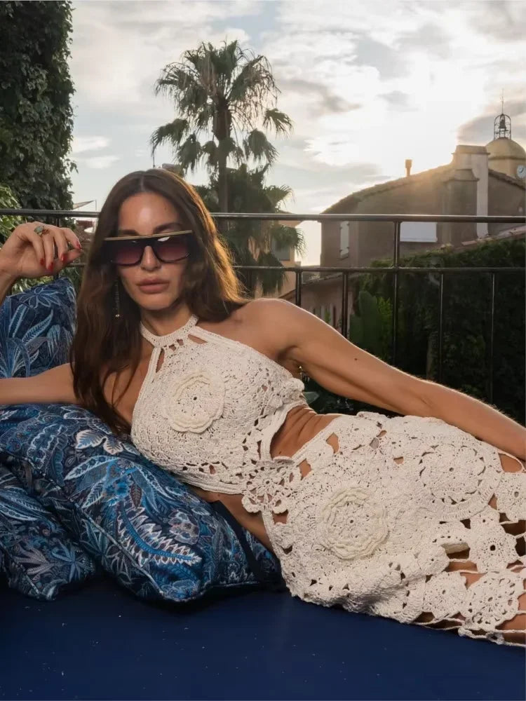 Woman in a white crochet outfit and sunglasses lounging outdoors.