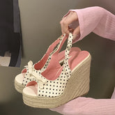 White wedge sandals with black polka dots held by a person wearing a pink sweater.