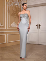 Woman in a strapless silver evening gown standing in an elegant room with a chandelier.