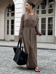 Woman in a brown dress holding a black bag on a stone pavement.