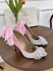 Pink high-heeled shoes with lace and crystal details on a wooden table.