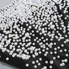 White pearls scattered on a black fabric background