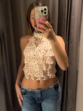 Person wearing a polka dot halter top and jeans, taking a mirror selfie.