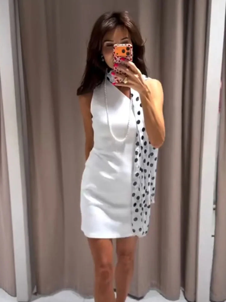 Woman taking a mirror selfie wearing a white halter neck dress with a polka dot overlay.