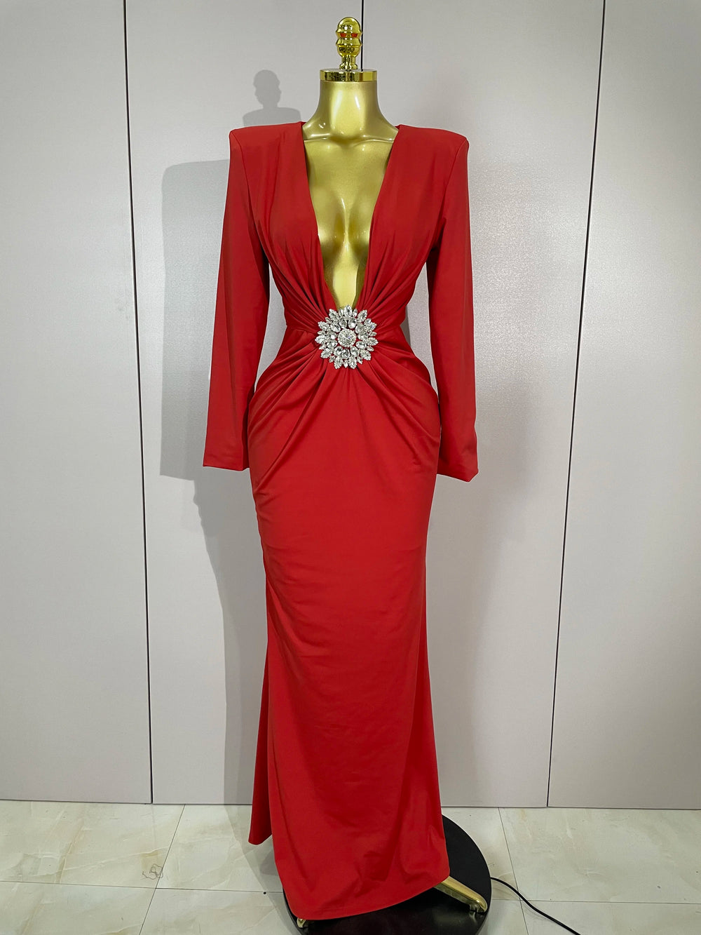 Red evening gown with a large brooch on a mannequin against a white background