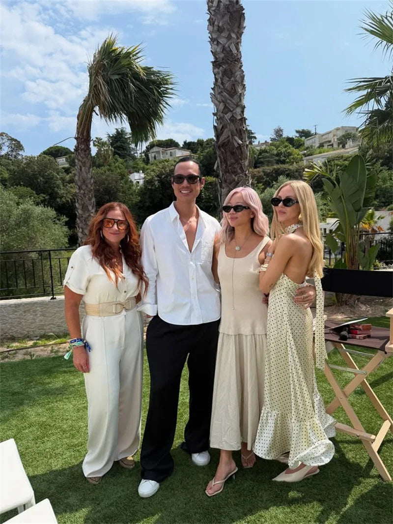 Group of four people posing outdoors with palm trees and a clear sky in the background