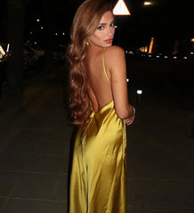 Woman in a yellow dress with an open back standing on a street at night.
