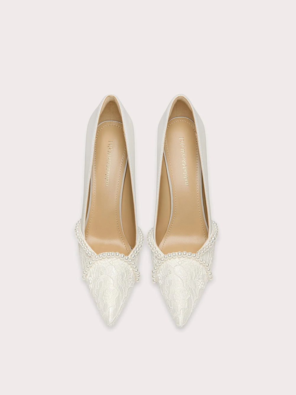 Pair of white pointed-toe shoes with lace detailing on a light gray background