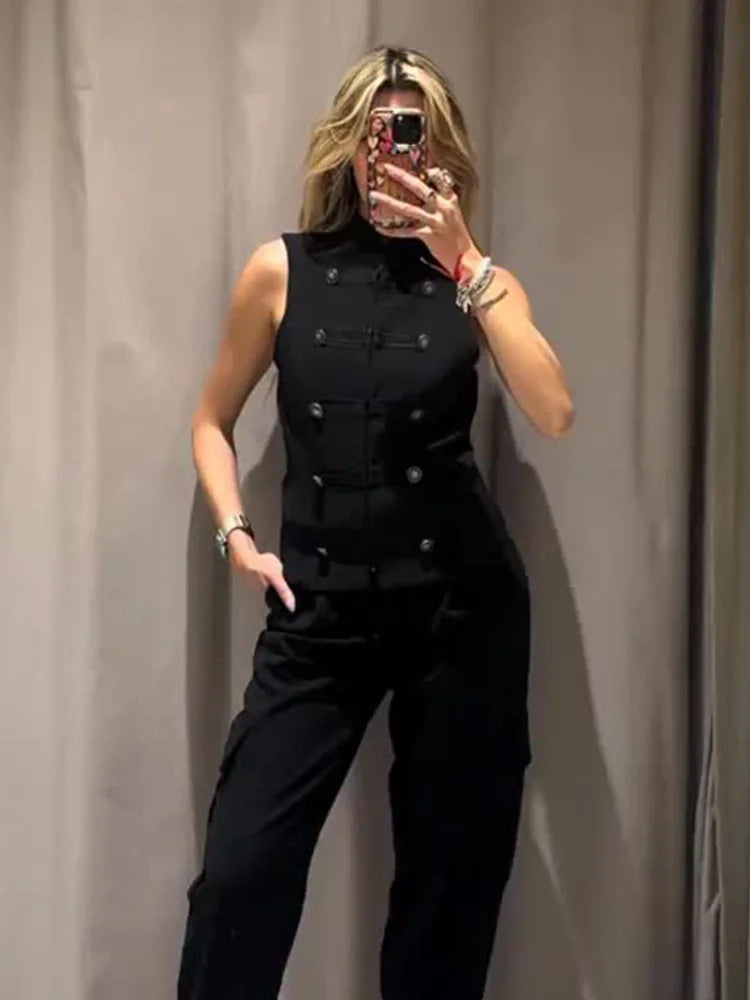 Person wearing a black sleeveless top with buttons and black pants against a plain background