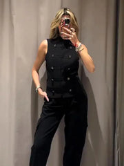 Person wearing a black sleeveless top with buttons and black pants against a plain background