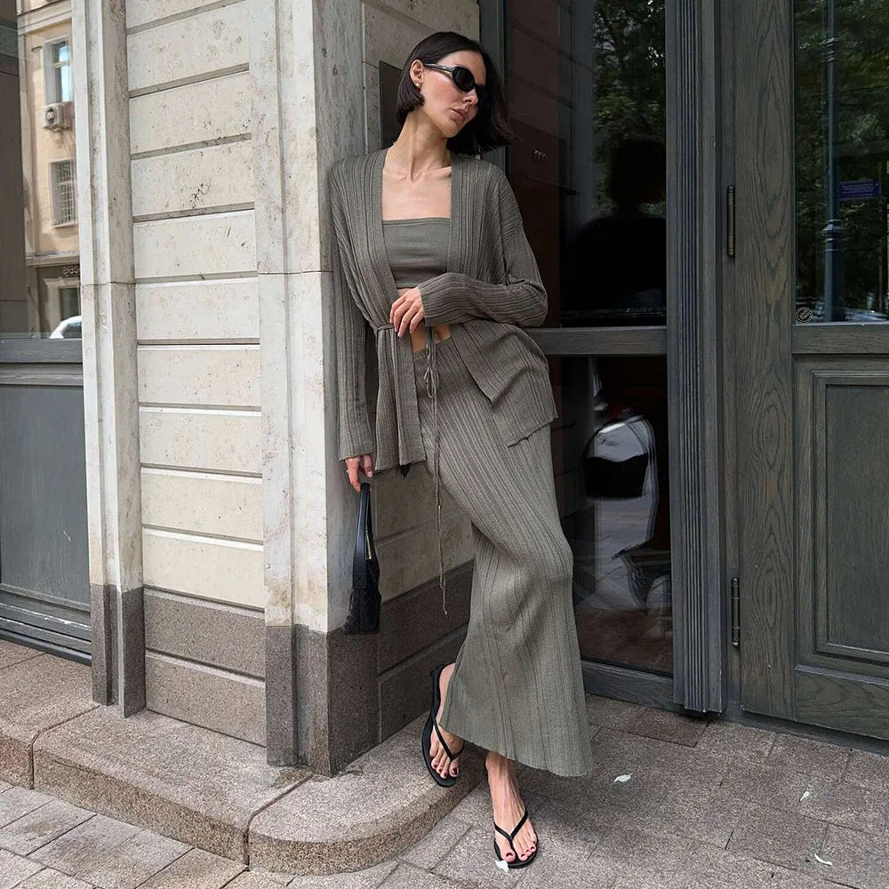 Woman in a gray outfit standing outside a building entrance.