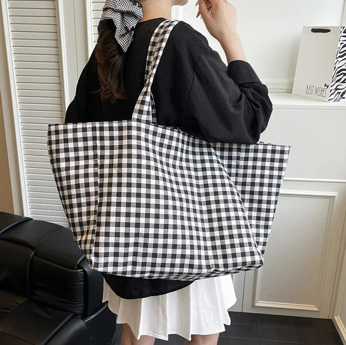 Person holding a black and white checkered tote bag in a room.
