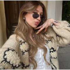 Woman wearing a beige knitted cardigan with black patterns, posing outdoors.