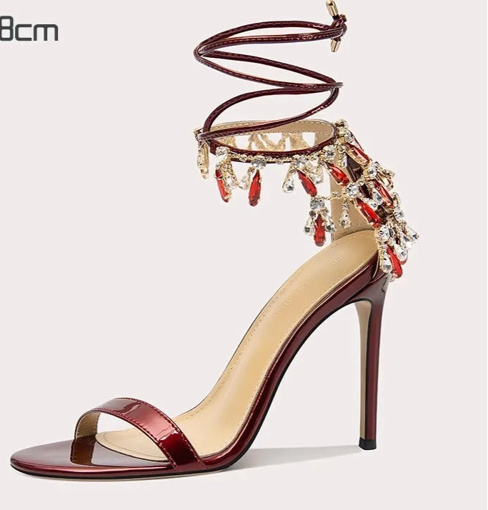 Red high-heeled sandal with decorative straps and crystals on a light background