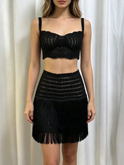 Woman standing in a black crocheted square neck crop top and fringe mini skirt.