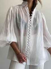White sheer blouse with button details worn by a person against a plain background