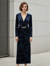 Woman wearing a dark blue velvet dress with a gold belt against a gray tiled wall.