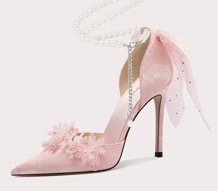 Pink high-heeled shoe with floral details and a chain on a white background