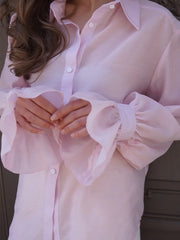 Close-up of a person wearing a light pink blouse with ruffled sleeves.