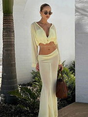 Woman in a light yellow outfit standing outdoors with a palm tree in the background