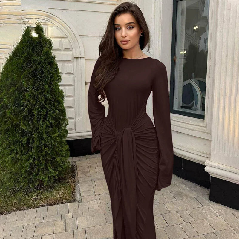 Woman in a brown dress standing outdoors next to a building.