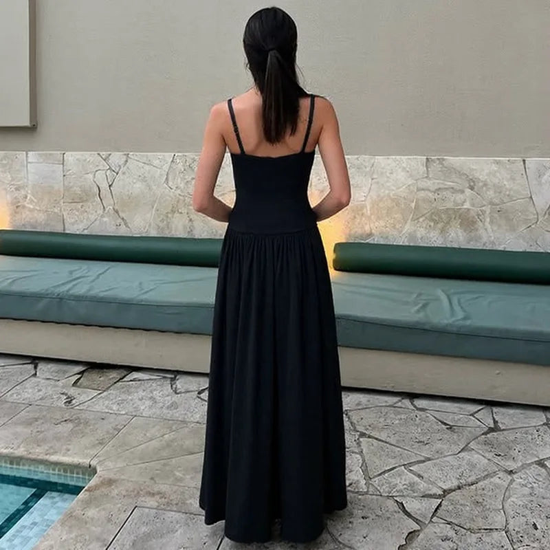 Woman in a black dress standing by a poolside.