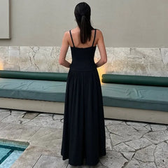 Woman in a black dress standing by a poolside.