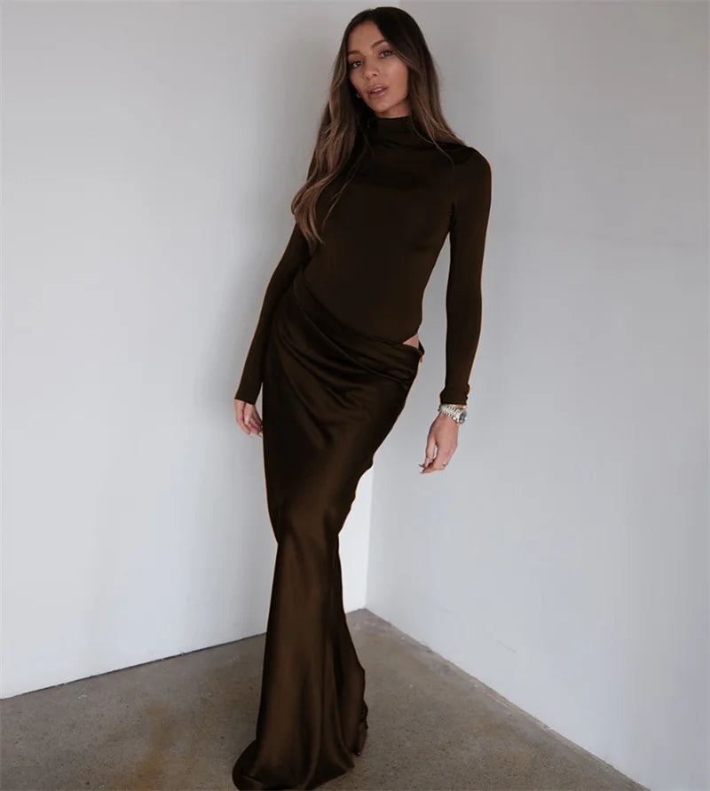 Woman wearing a brown long-sleeve dress against a plain white wall.
