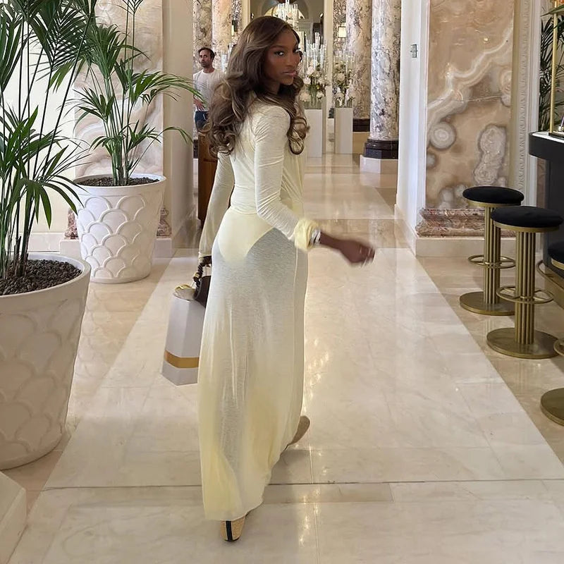 Woman in a long, light-colored dress walking in an elegant interior setting with marble floors and decorative plants.