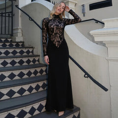 Woman in a black lace dress standing on a staircase with a white wall and black railing.
