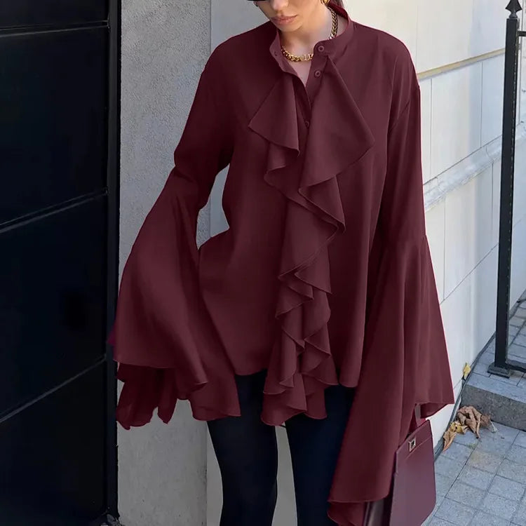 Person wearing a burgundy ruffled coat standing against a building wall.