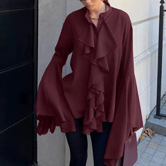 Person wearing a burgundy ruffled coat standing against a building wall.