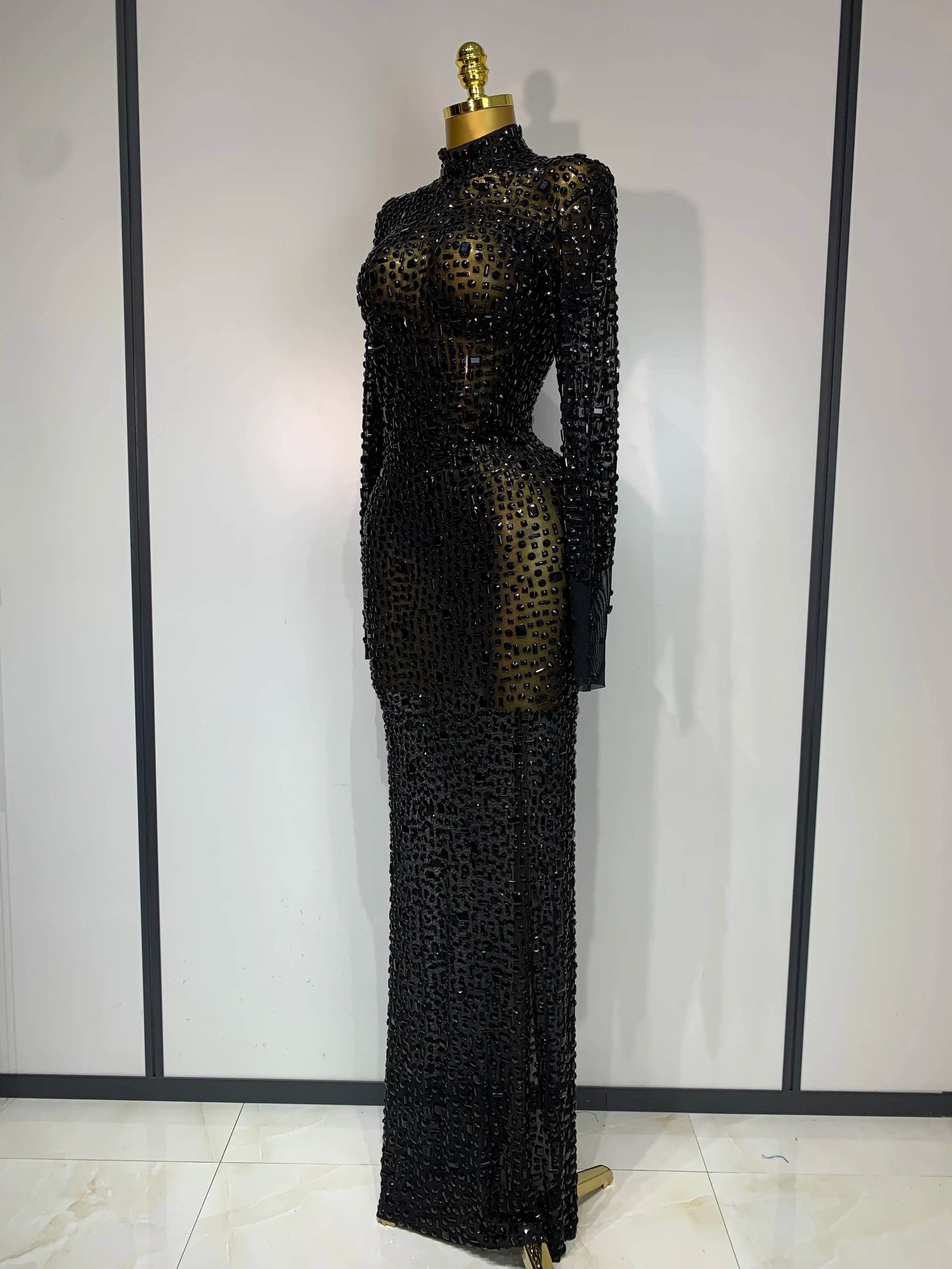 Black beaded evening gown on a mannequin against a white wall.