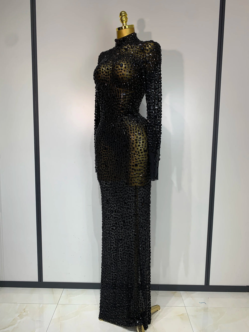 Black beaded evening gown on a mannequin against a white wall.