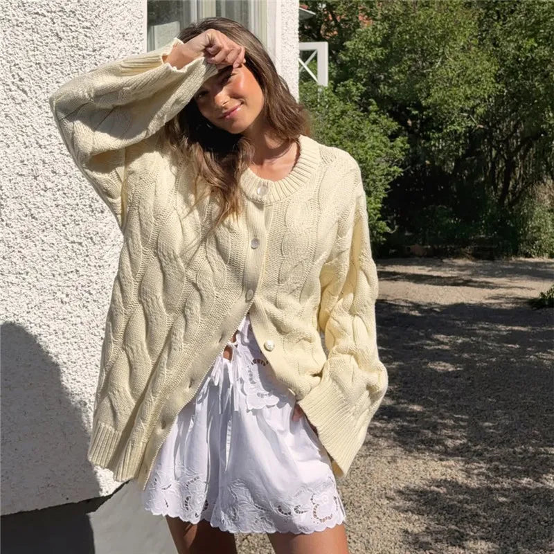 Woman wearing a light green cable knit cardigan over a white dress, standing outdoors.