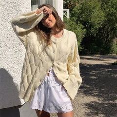 Woman wearing a light green cable knit cardigan over a white dress, standing outdoors.