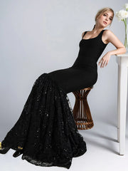 Woman in a black dress with a flowing skirt sitting on a stool against a white background