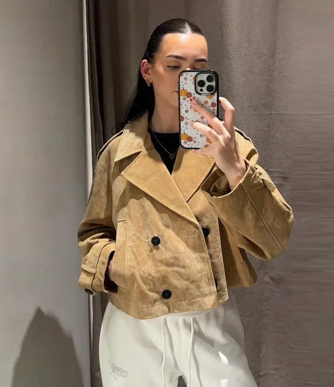 Person wearing a beige jacket taking a mirror selfie against a plain background