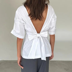 White blouse with a bow detail on the back worn by a person against a neutral background