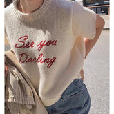 Person wearing a cream-colored sweater with red text 'See you Darling' in an urban setting.