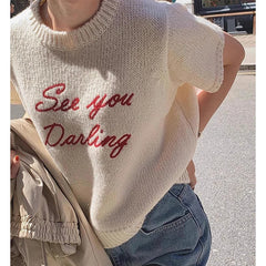 Person wearing a cream-colored sweater with red text 'See you Darling' in an urban setting.