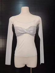 Mannequin wearing a white top with sheer sleeves and a silver embellished section against a dark background.