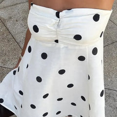 White strapless top with black polka dots worn by a person on a pavement background
