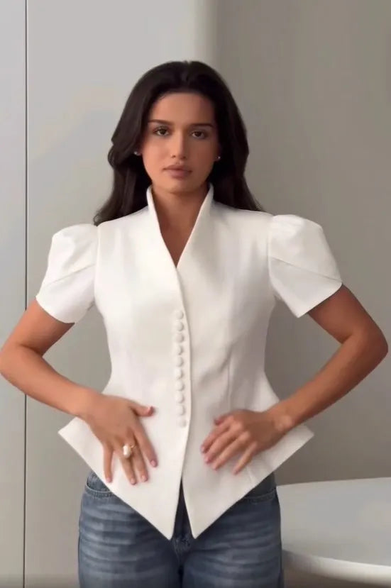 Woman wearing a white blouse with short sleeves and blue jeans against a neutral background