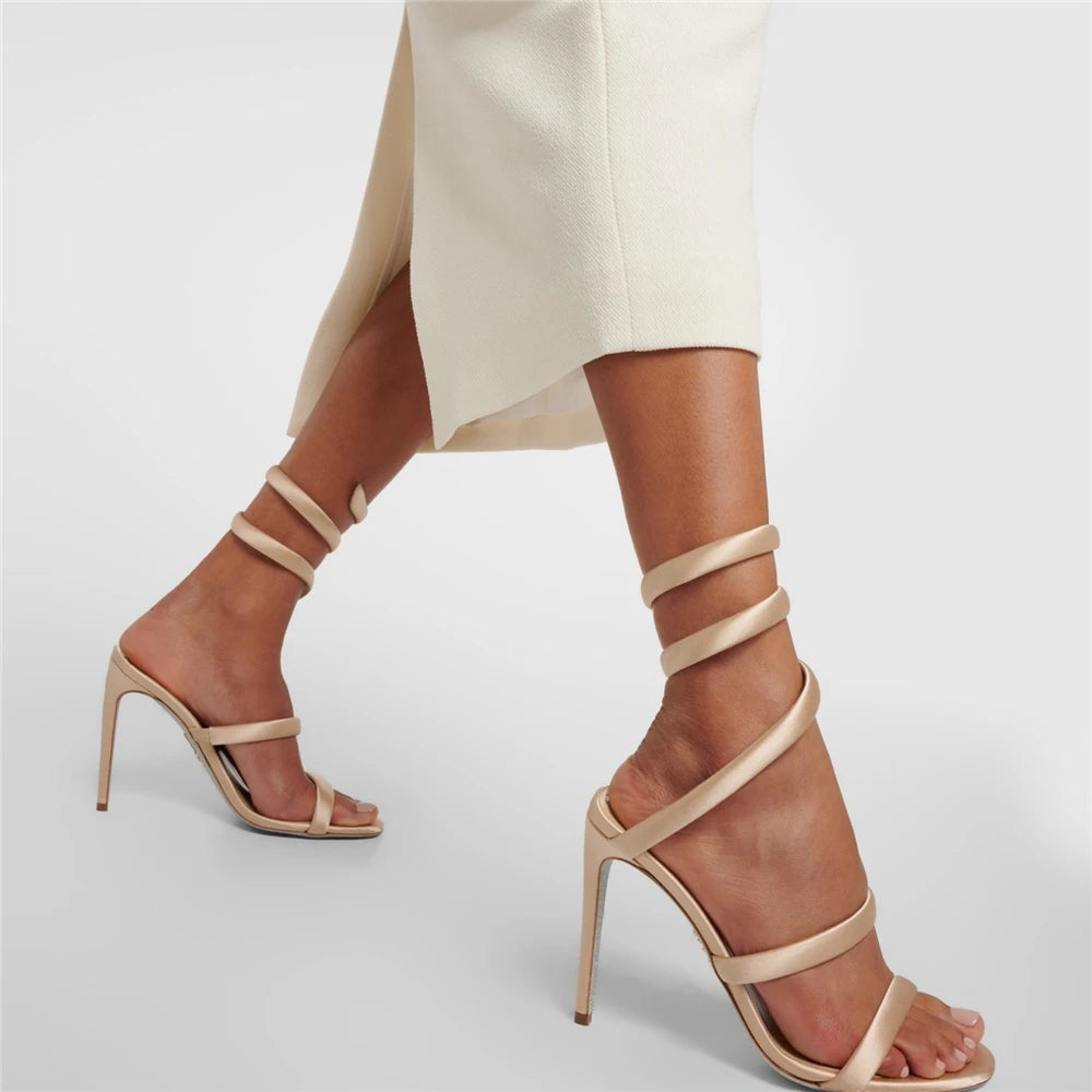 Beige high-heeled sandals worn with white pants on a light gray background